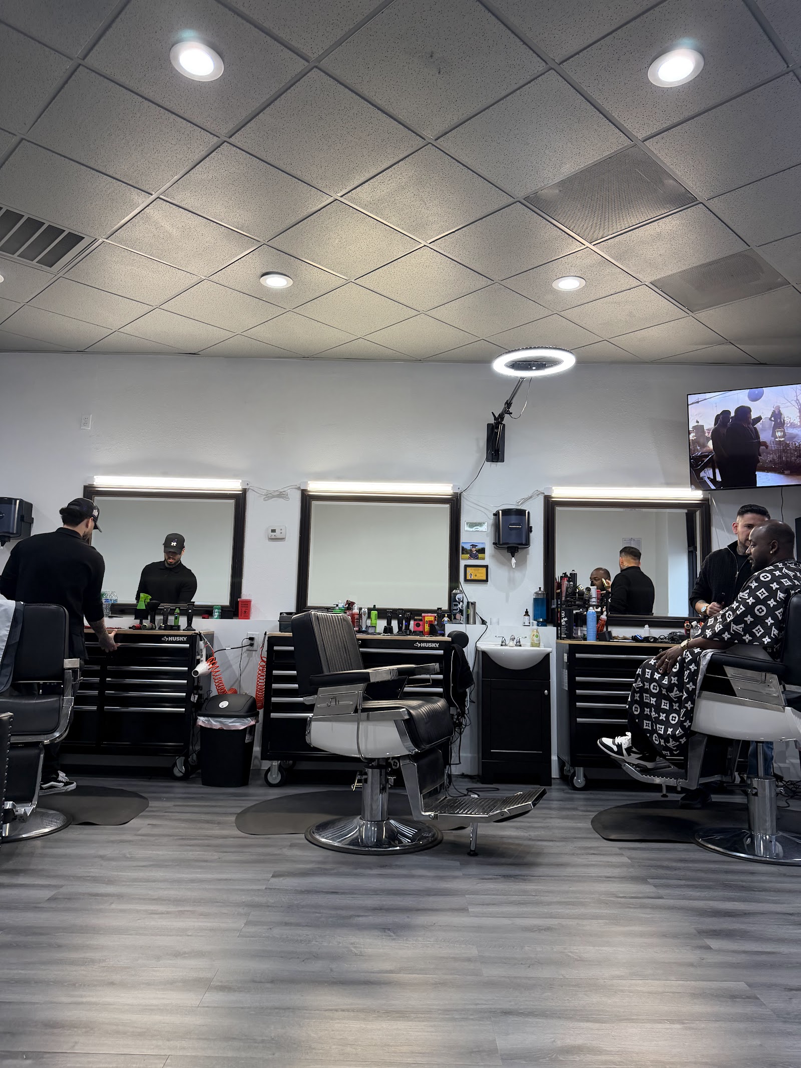 Interior of the barbershop with multiple barbers working at stations, clients in chairs and a TV on the wall