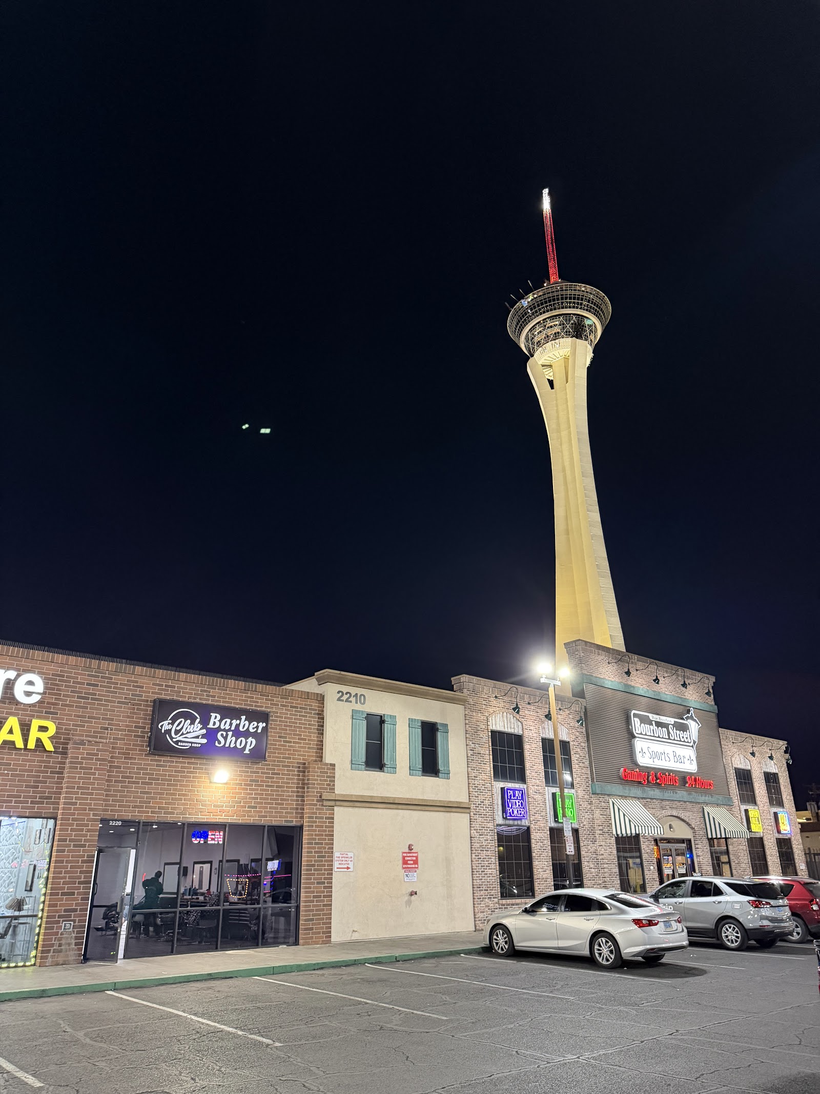 The Club Barber Shop exterior at night with the Strat tower lit up in the background